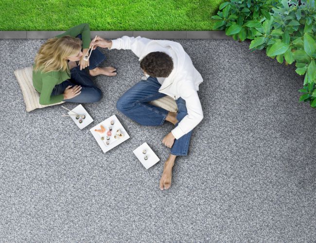 Couple sitting on patio decking, eating sushi with chopsticks, overhead view